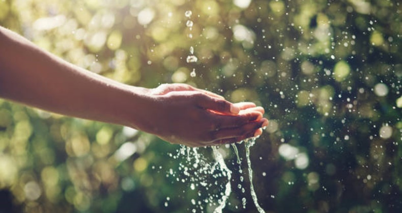 Closeup shot of a man holding his hands under a stream of water outdoors